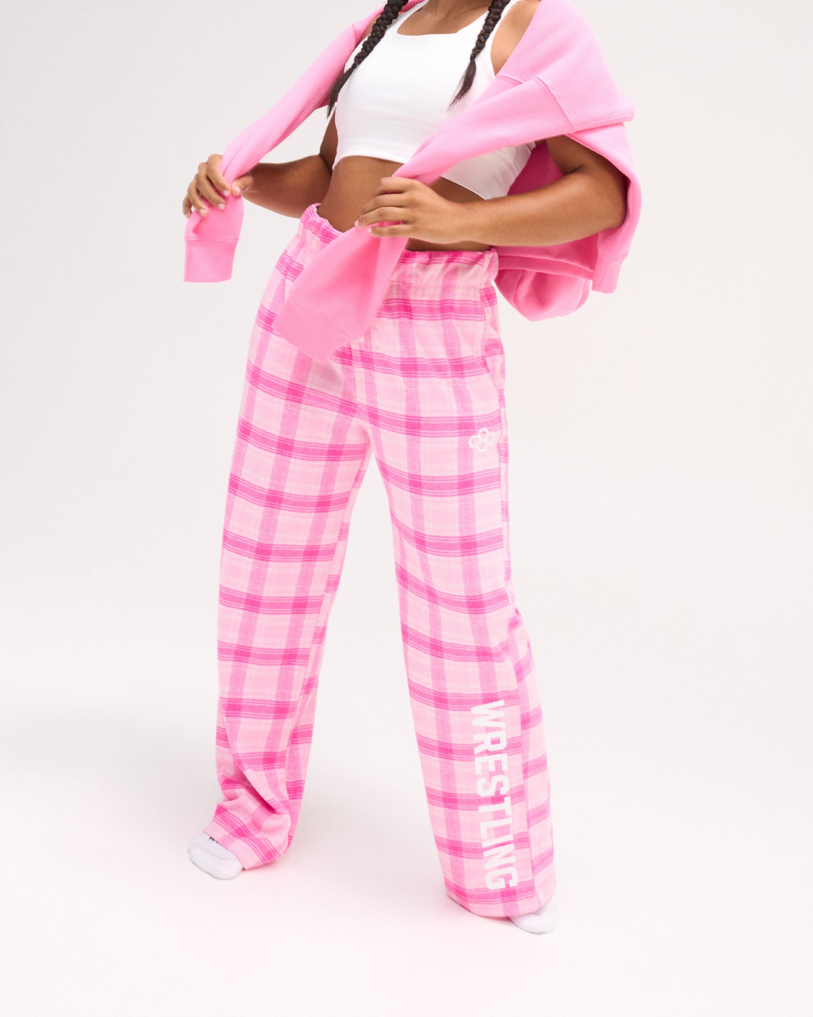 Female model wearing RUDIS Hex Flannel Lounge Pants in Pink plaid with a relaxed wide-leg silhouette, white RUDIS hex logo and WRESTLING leg lettering. Copy Alt Text