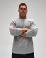 A man wearing a heather gray long-sleeve athletic shirt with a small black logo on the left chest, standing with arms crossed against a light gray studio background.