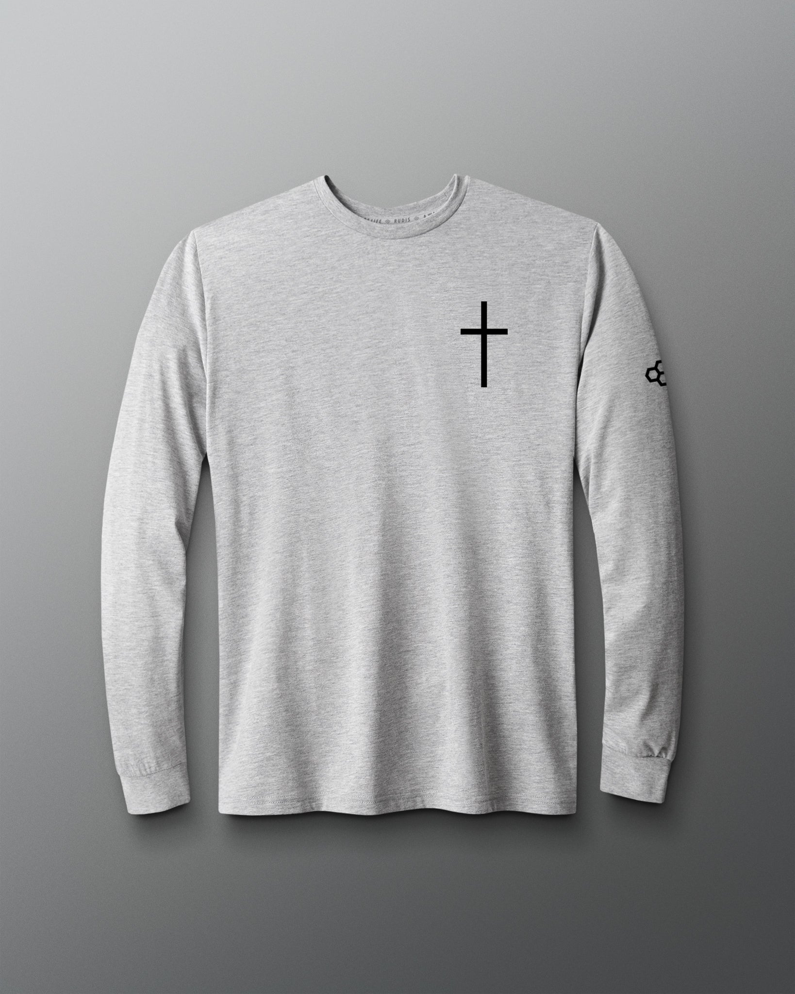 A light gray heather long-sleeve t-shirt with a black cross printed on the left chest and a small black logo on the right sleeve, displayed against a dark gray gradient background.