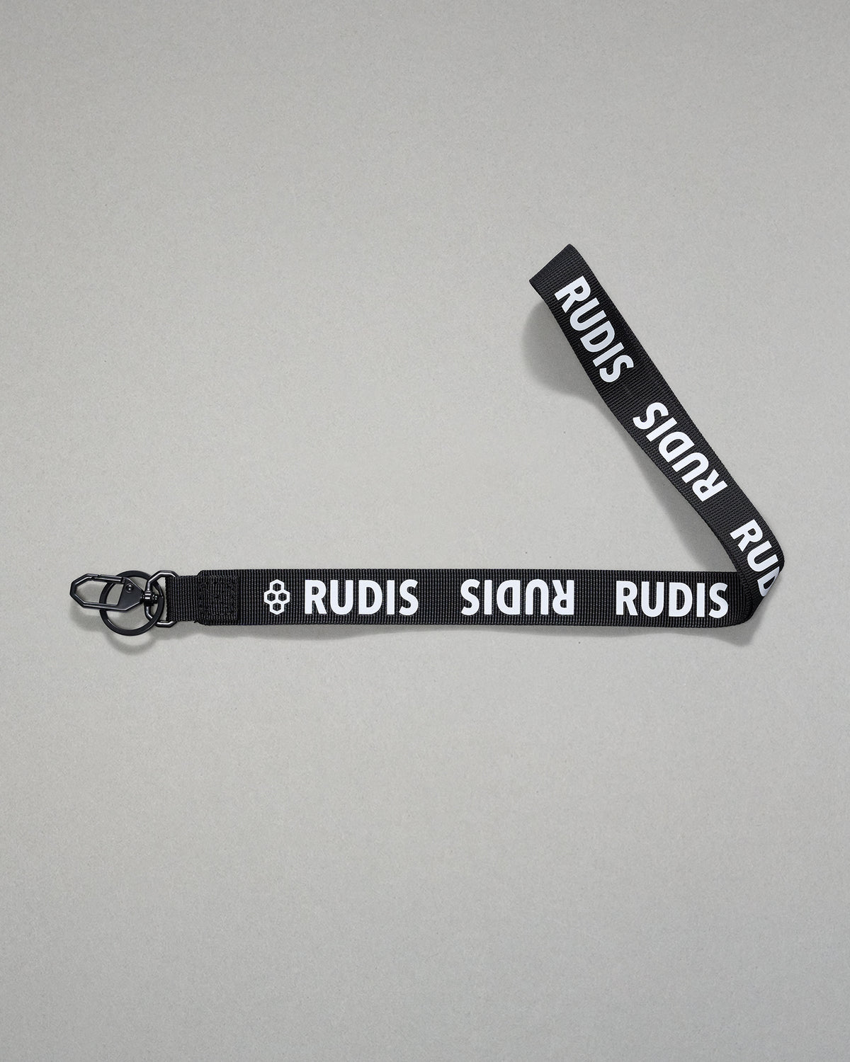 Black RUDIS Wordmark lanyard with repeating white RUDIS logos, woven polyester strap, metal key clip, and key ring for carrying keys, badges, or accessories.