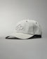 A light gray baseball cap with an embroidered hexagonal logo is displayed at an angle against a muted gray background, highlighting its structured design and comfortable fabric.