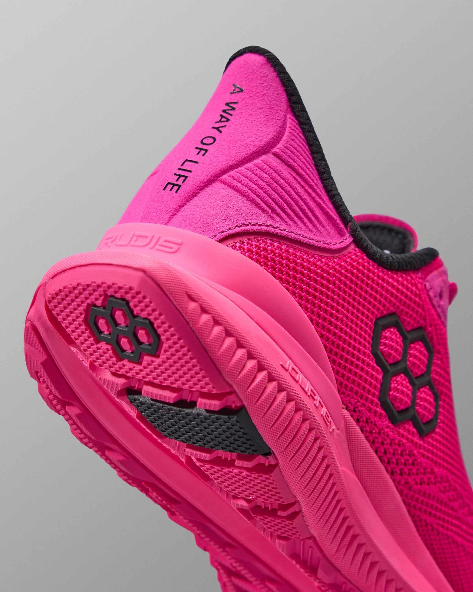 Pink athletic shoe with black text and logo on a gray background with black RUDIS logo
