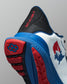 Close-up rear view of a white RUDIS training shoe featuring a red and blue USA Wrestling logo on the side, red ‘A WAY OF LIFE’ text on the black heel tab, and a blue and red outsole with hexagon tread detail.