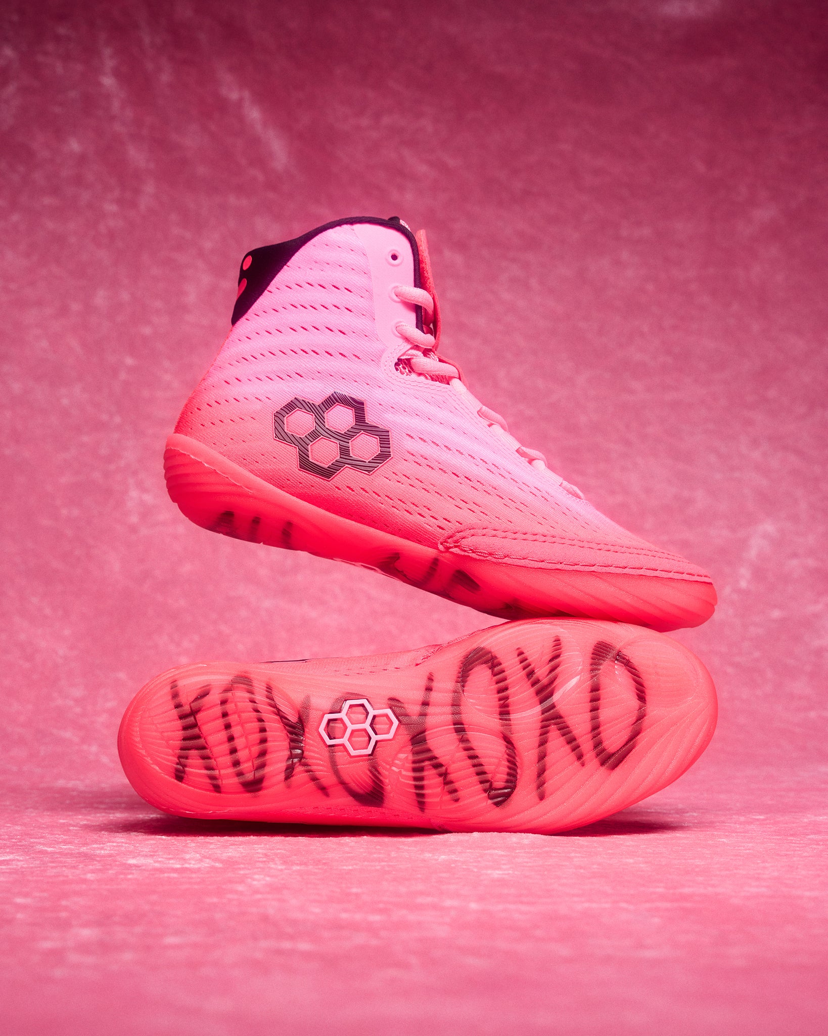 Pink wrestling shoes with black text and logo on a pink background