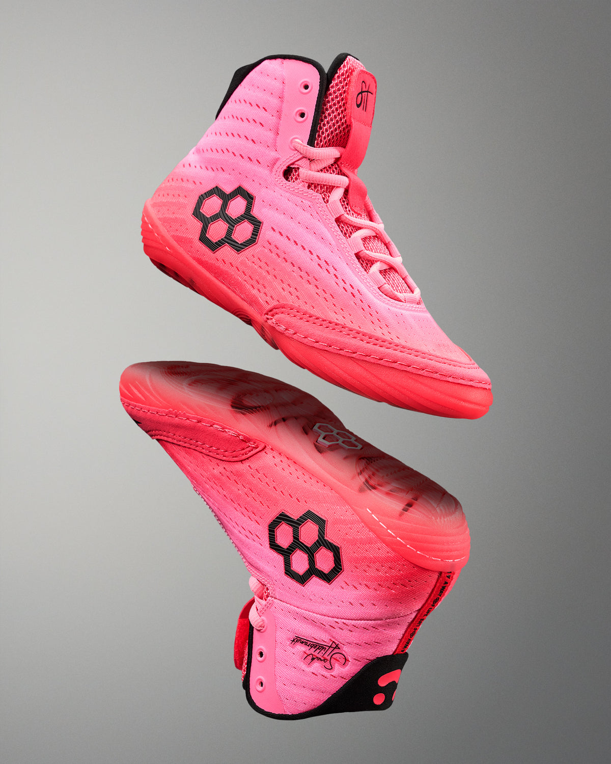 Pink wrestling shoes with black hexagonal logo on a gray background