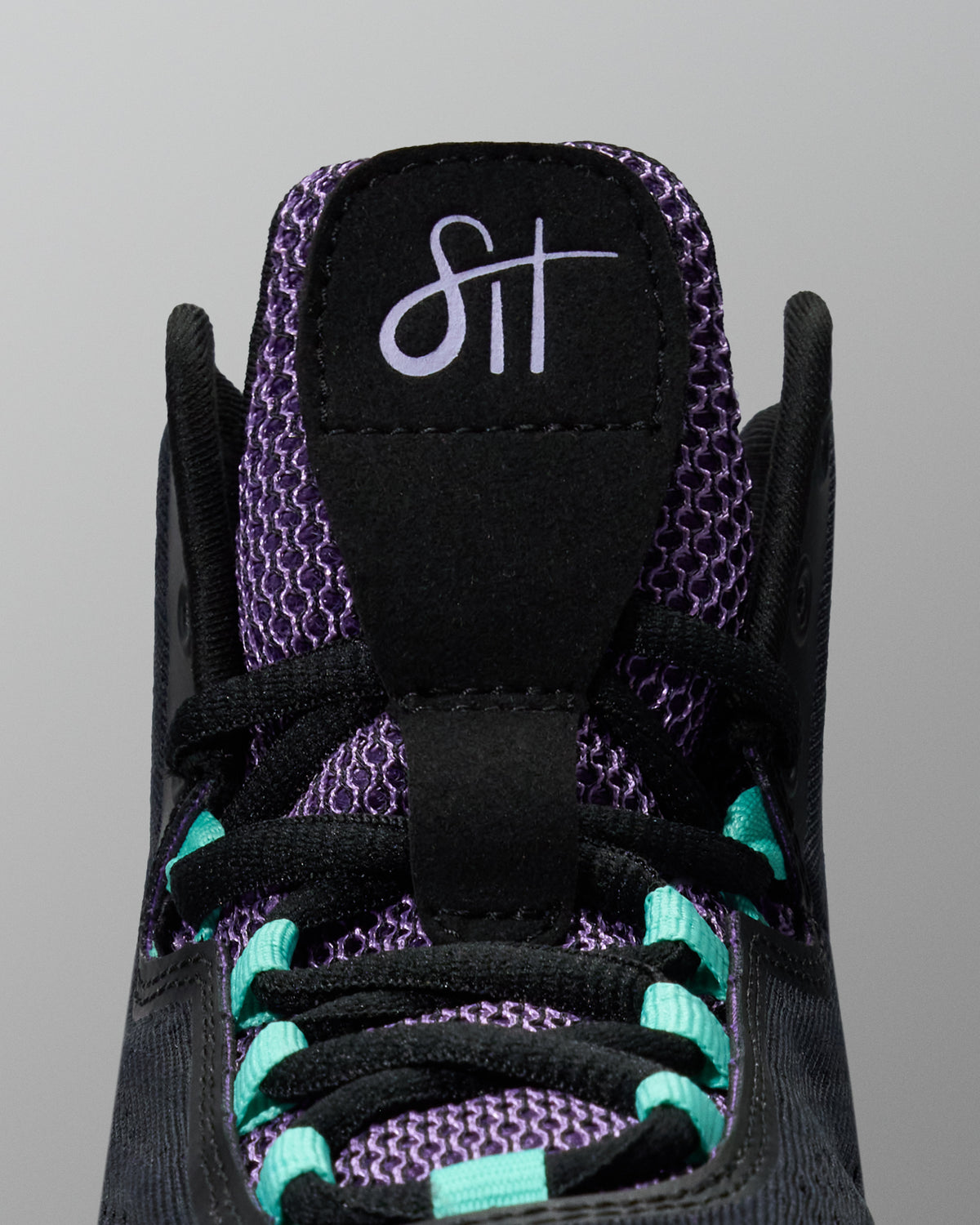 Close-up of a black sneaker with purple and teal accents on a gray background