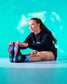 Person wearing black sweatshirt and colorful socks sitting on a light blue floor with a teal gradient background.