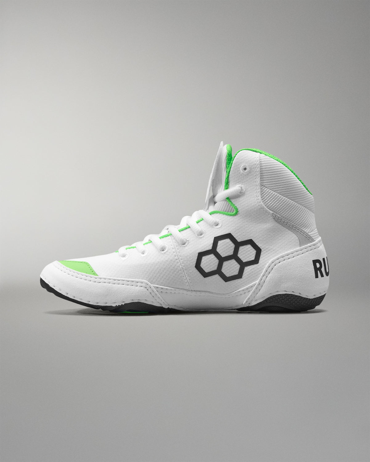 White wrestling shoes with green accents and a black logo on a gray background