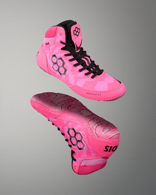 A pair of bright pink high-top athletic Wrestling shoes with black laces and black geometric logo details, shown from the side and sole views against a neutral gray gradient background.