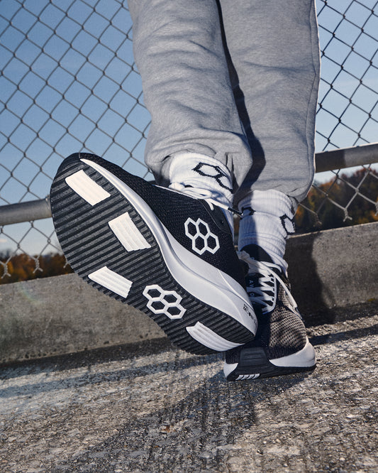 Black and white athletic shoes with brand logo on a concrete surface.