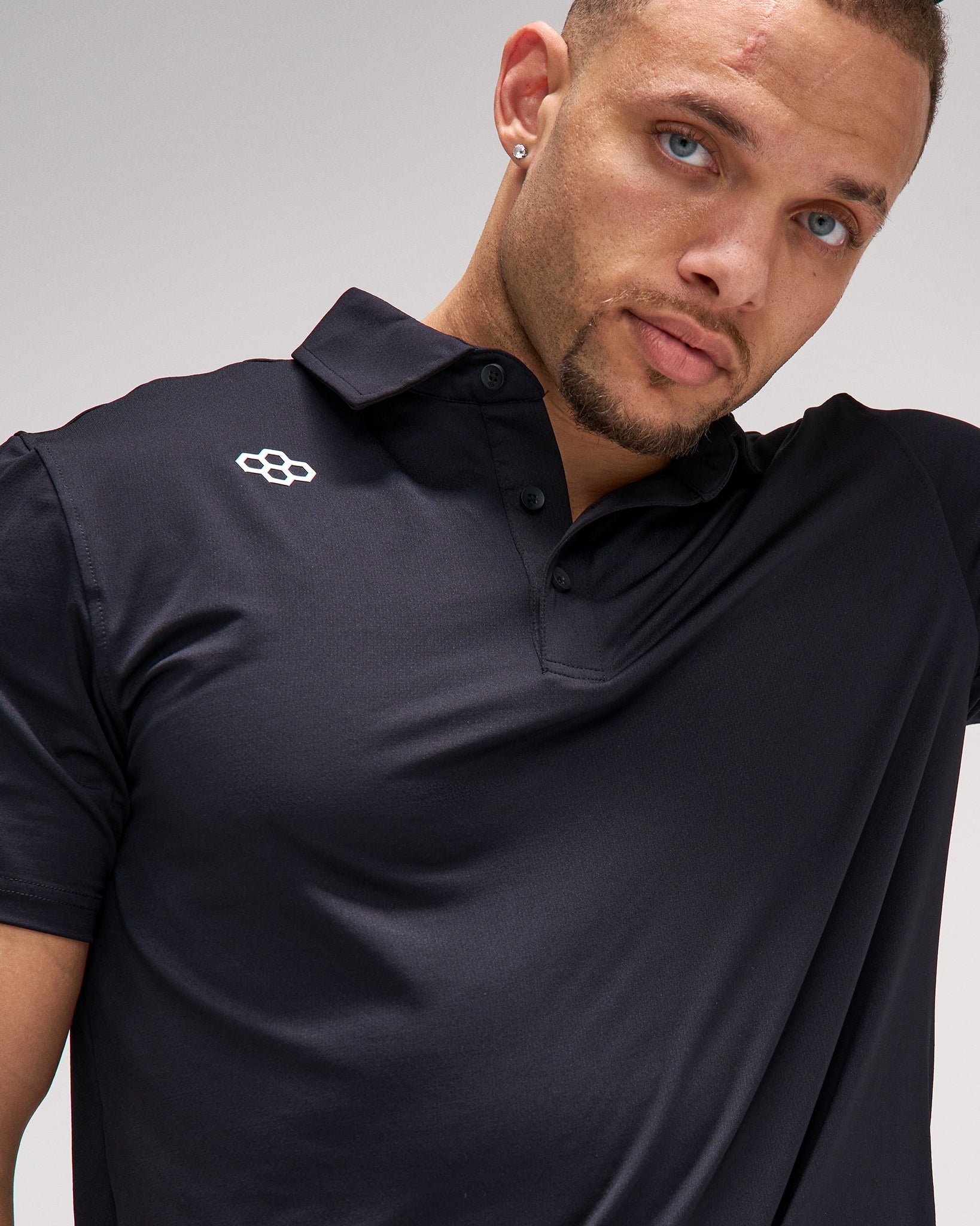 Man wearing a black polo shirt with a logo on a gray background