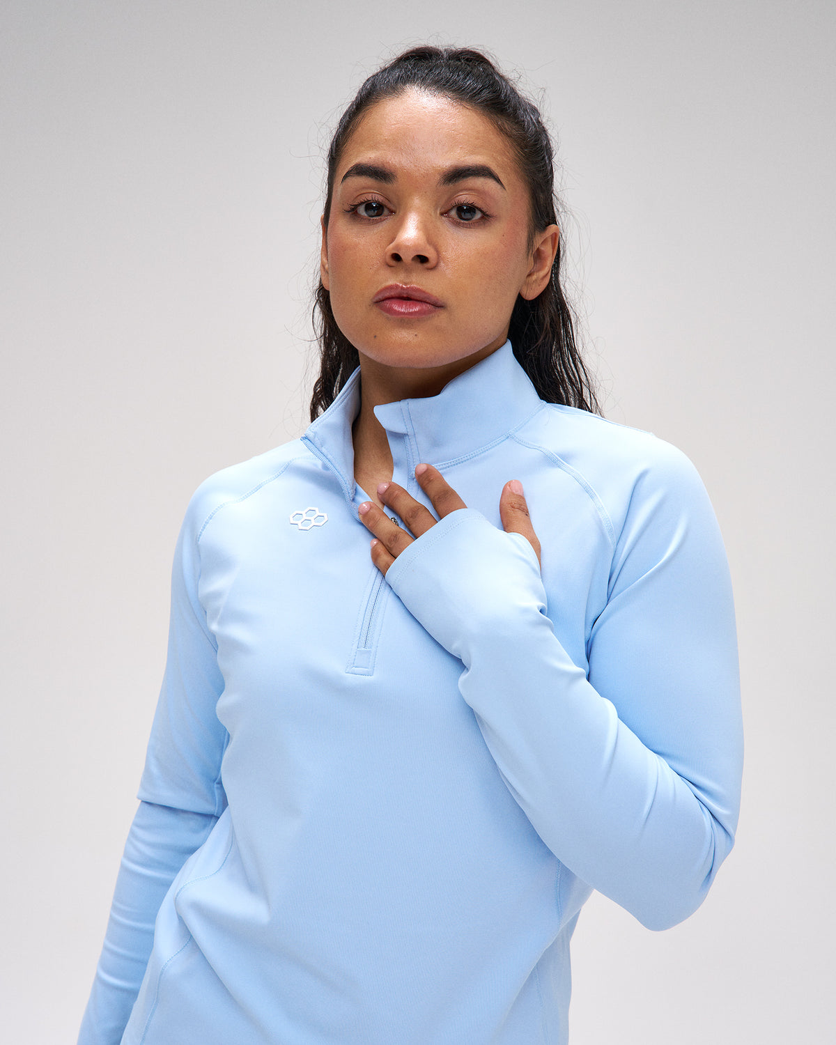 Woman wearing a light blue long-sleeve top with a brand logo on a plain background