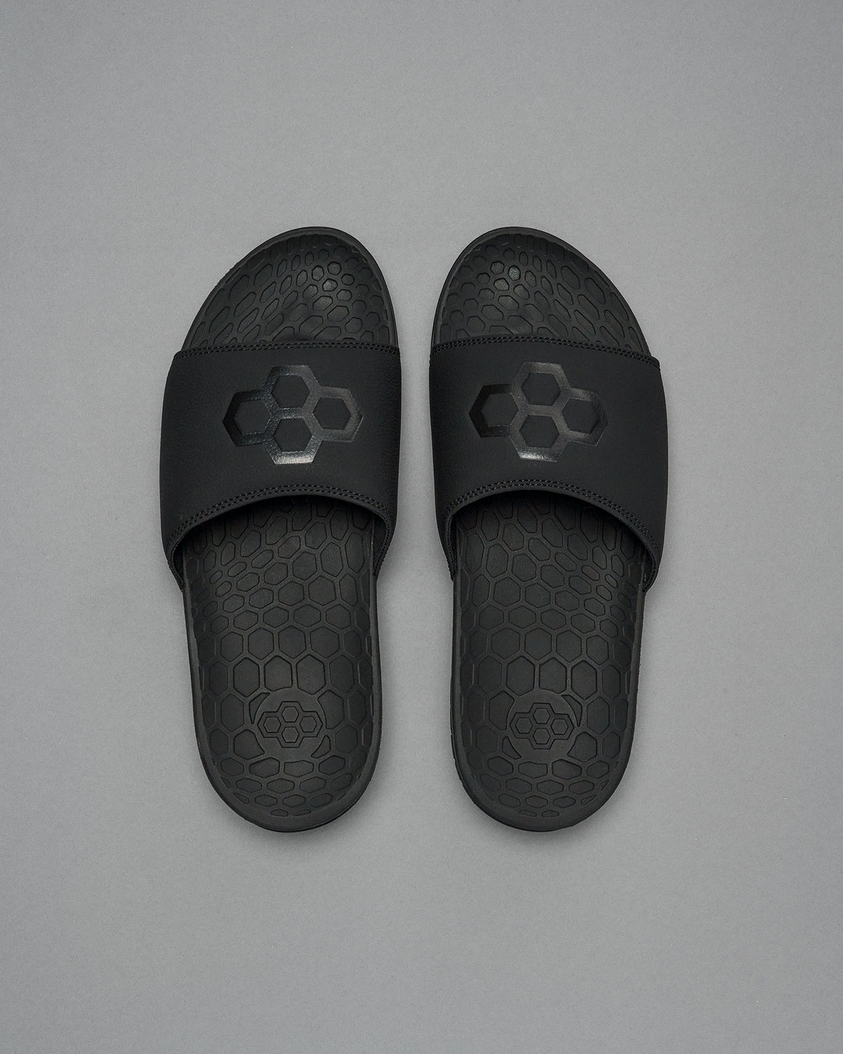A pair of black RUDIS Hex slides with the brand's logo on the strap, placed on a grey background.