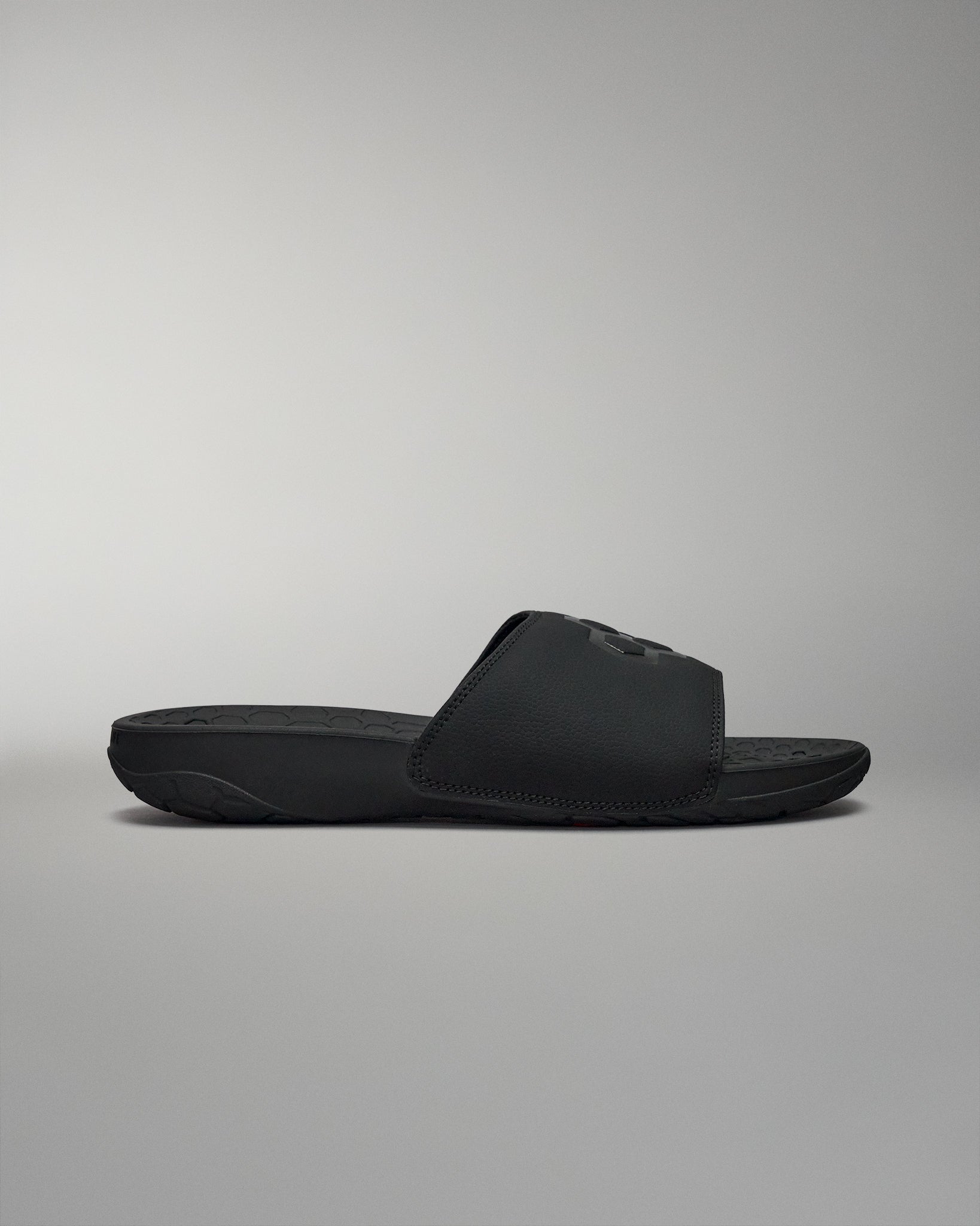Side view of black slides sandal shoes on grey background.