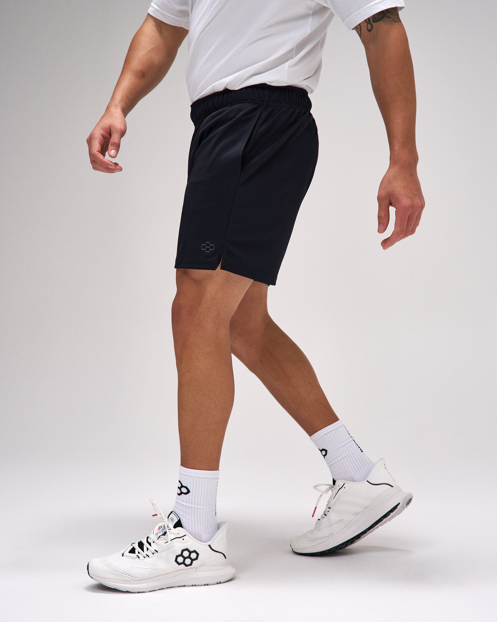 Person wearing black shorts, white socks, and white sneakers on a plain background