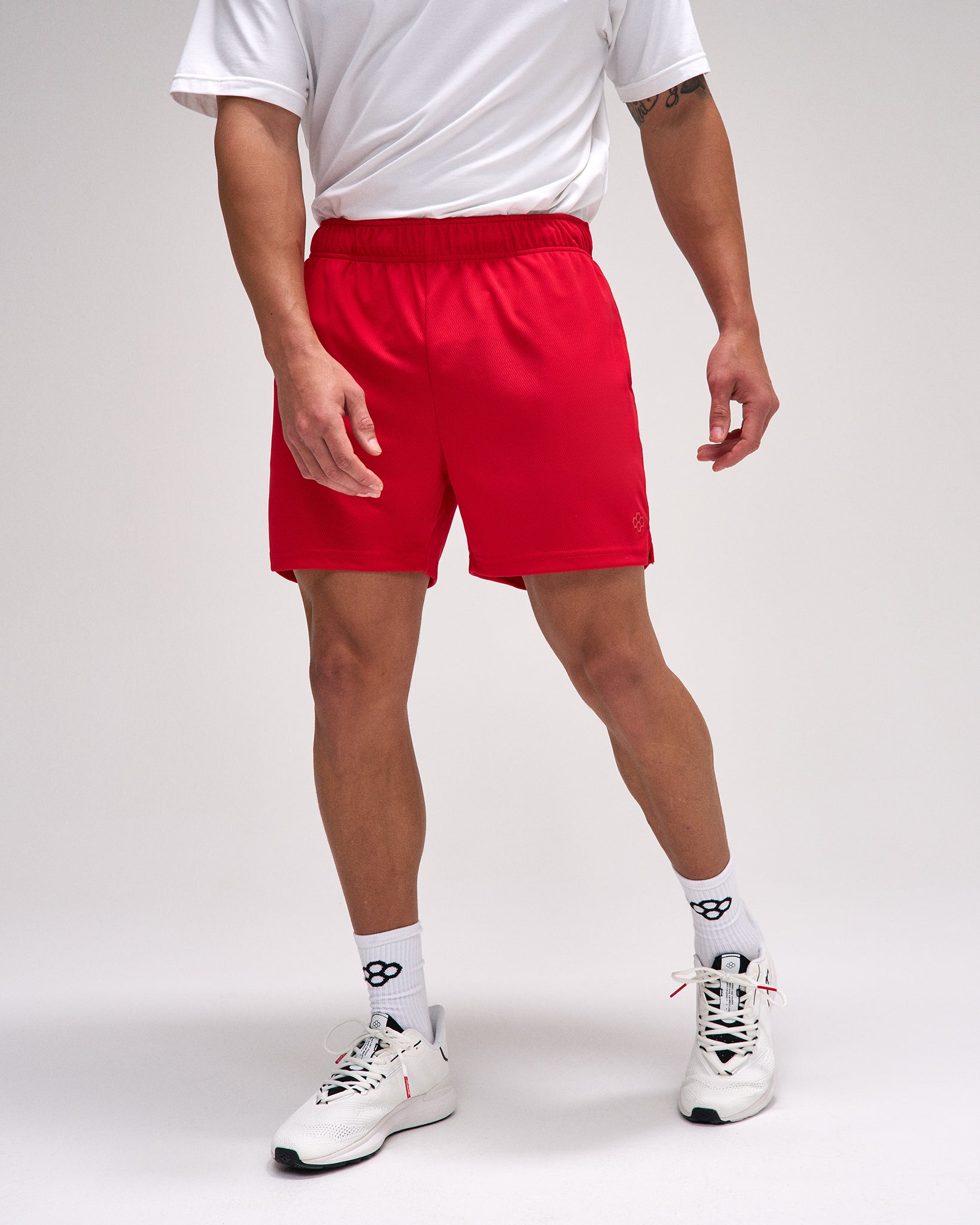 Person wearing red shorts, white t-shirt, and white sneakers on a plain background