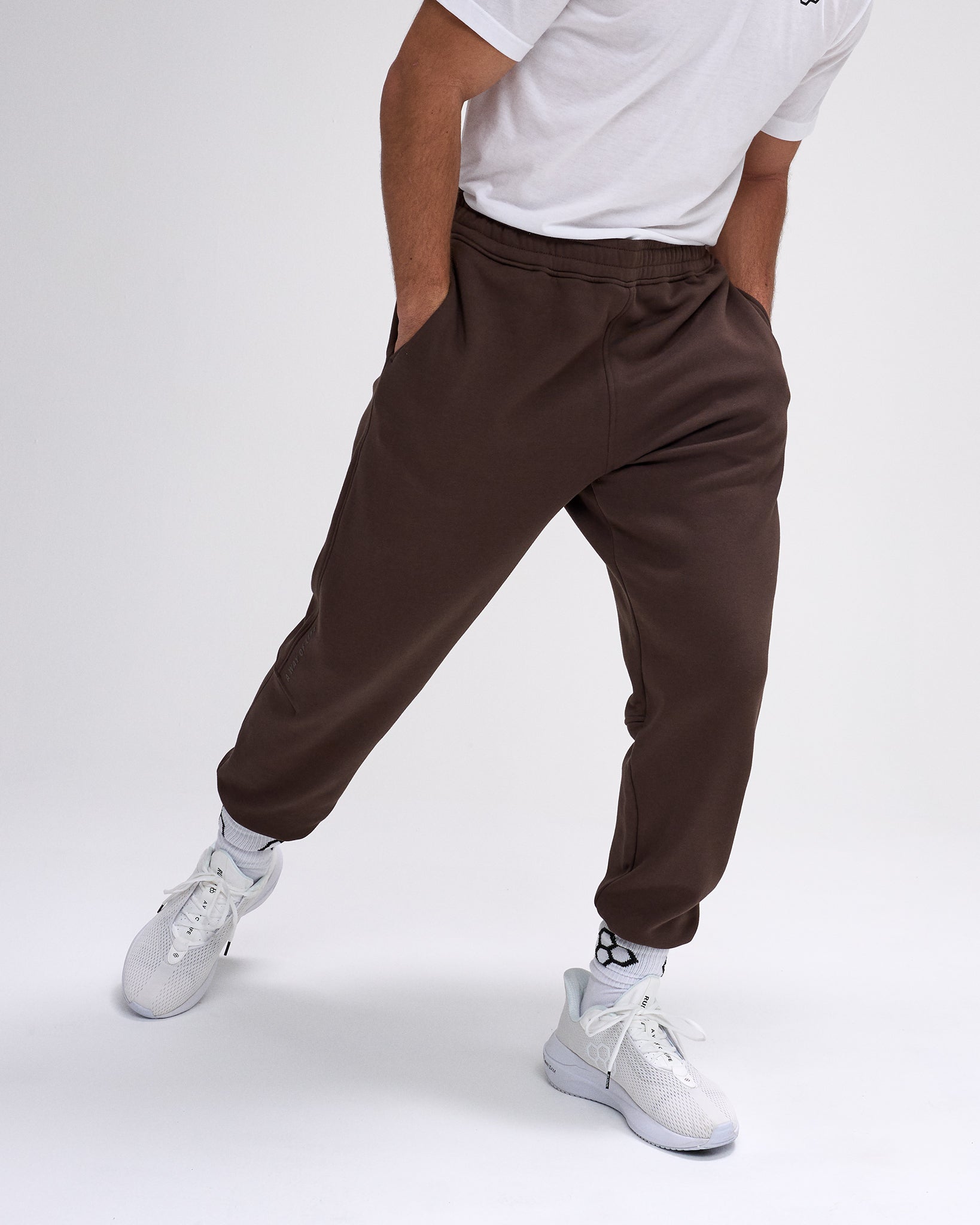 Person wearing brown jogger pants and white sneakers on a plain background