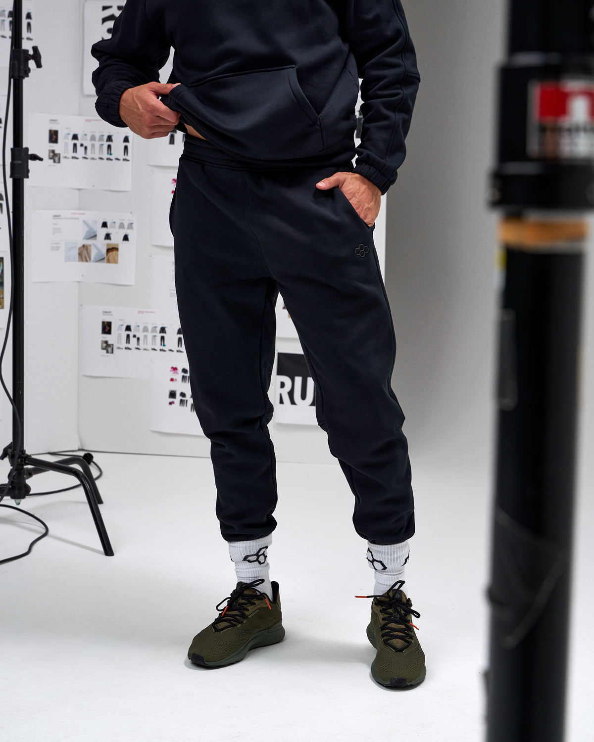 Person wearing a black outfit with white socks and green shoes in a studio setting.