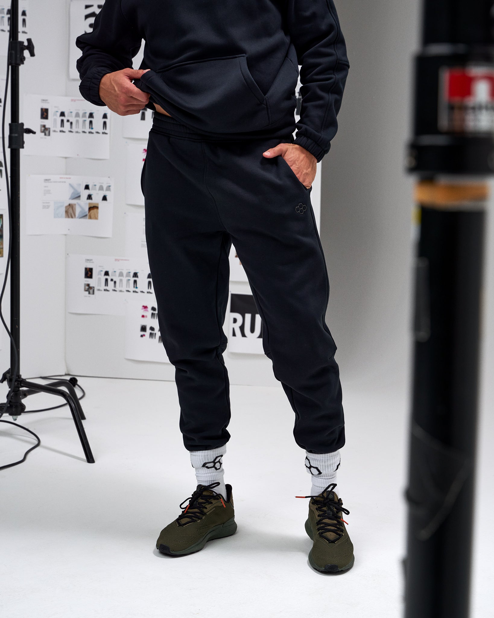 Person wearing a black outfit with white socks and green shoes in a studio setting.
