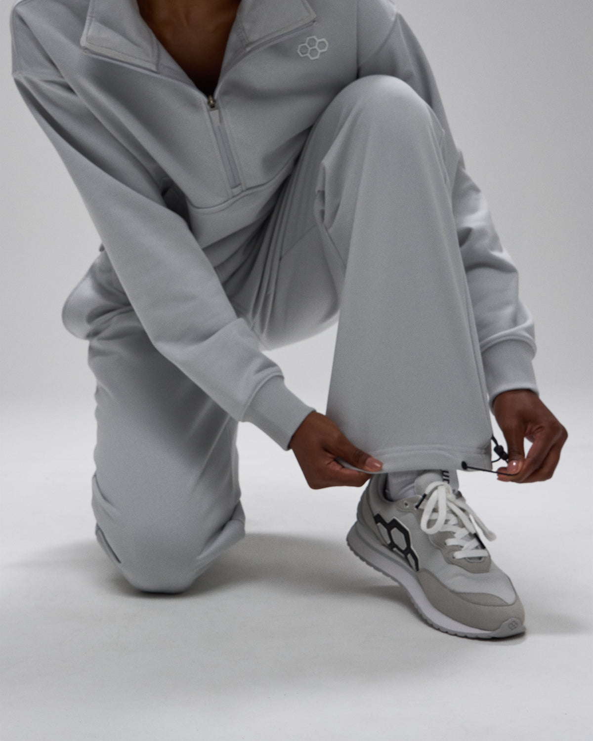 Person wearing a gray tracksuit with matching sneakers on a light gray background