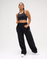 Female model wearing RUDIS Comfort Fleece Wide Leg Sweatpants in Black with a black athletic sports bra, showcasing the relaxed fit and adjustable drawstring waist. Copy Alt Text