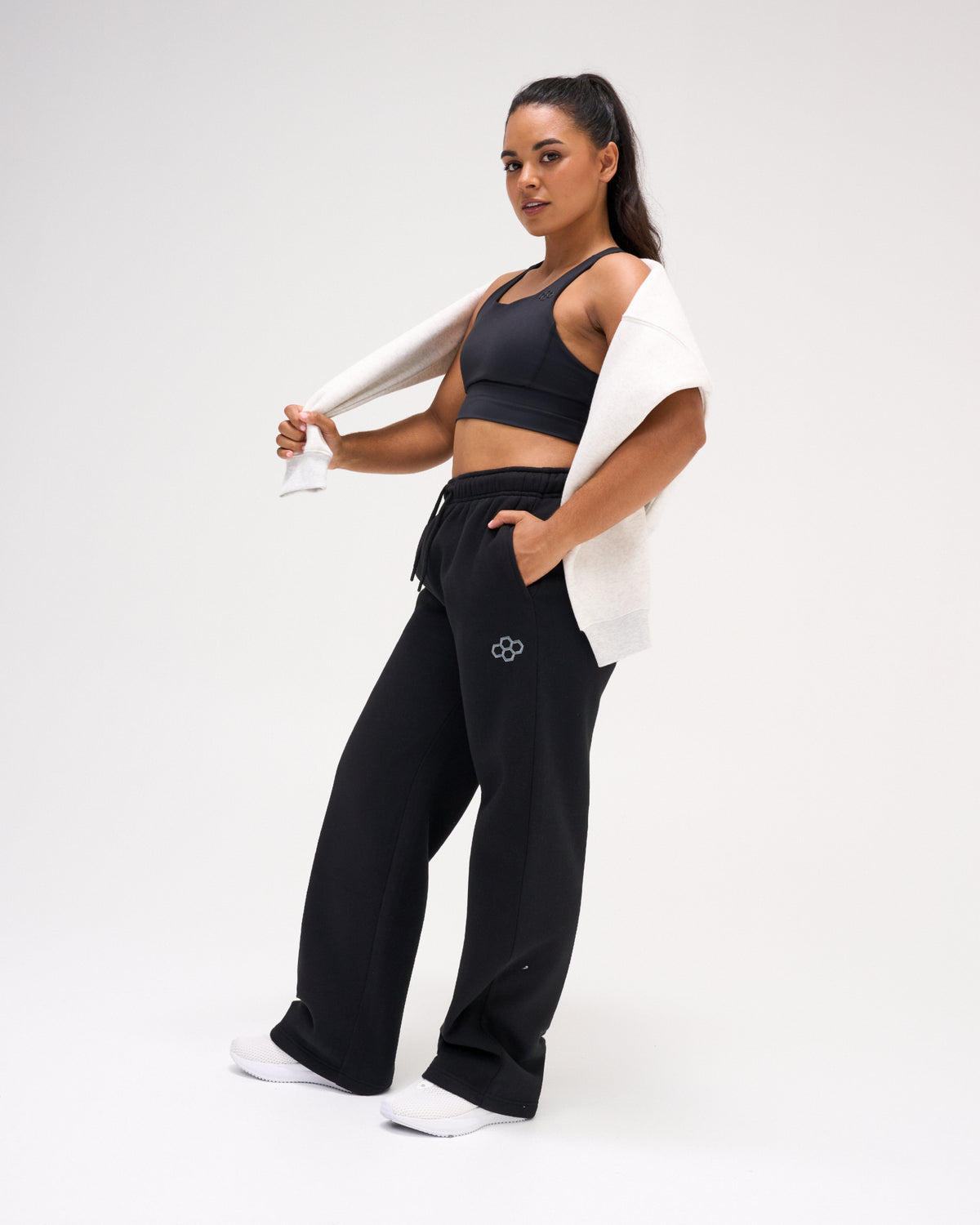Female model styling RUDIS Comfort Fleece Wide Leg Sweatpants in Black with a sports bra and draped sweatshirt, showing the relaxed silhouette and wide-leg fit. Copy Alt Text