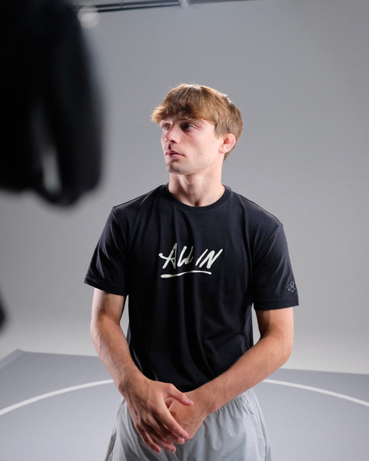 Person wearing a black t-shirt with 'ALL IN' printed on it, standing in a neutral setting.