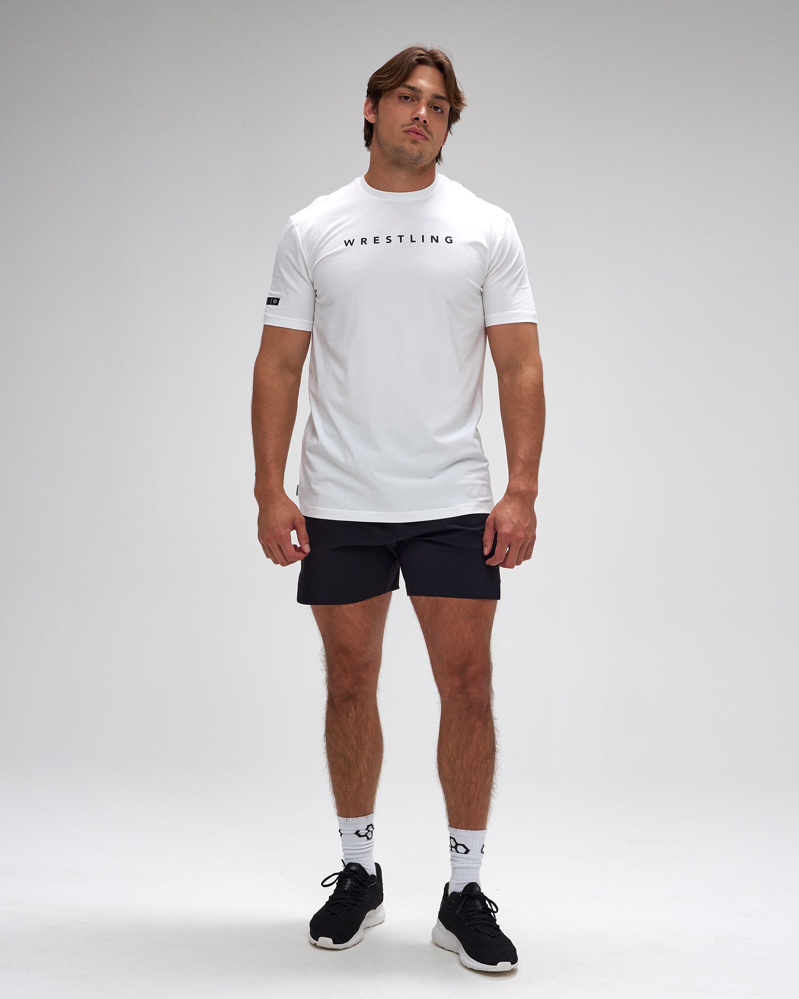 Man wearing a white 'Wrestling' t-shirt and black shorts on a gray background