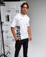 Man wearing a white t-shirt with 'RUDI' printed on it, standing in front of a white wall with graphics.