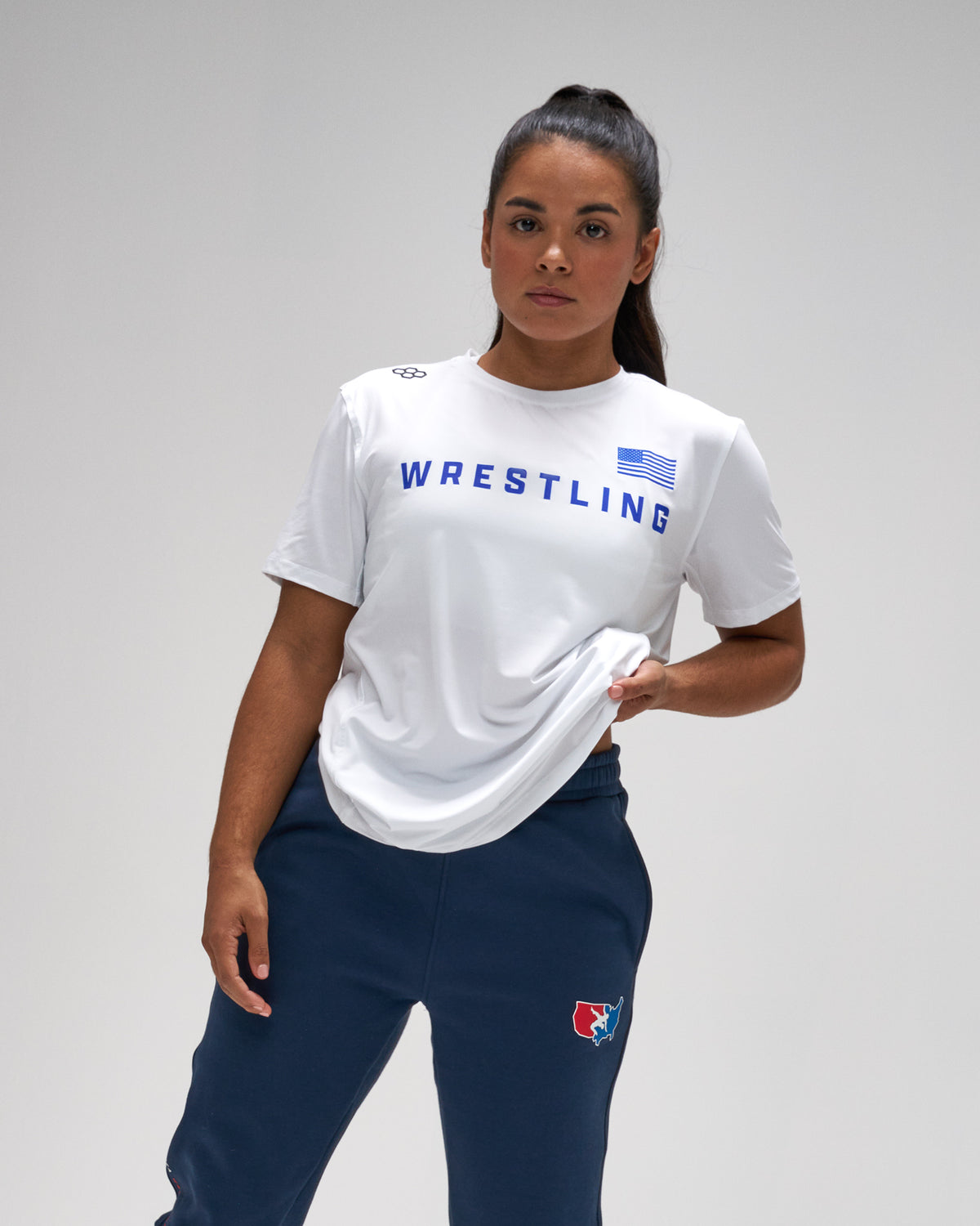 Person wearing a white 'Wrestling' t-shirt and navy pants on a gray background