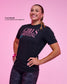Smiling female athlete wearing the RUDIS Girl Power Wrestling Elite Super Soft T-Shirt in black with pink "Girls Wrestling" graphic, paired with gray camo leggings in a pink studio.