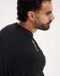 A close-up side profile of a man wearing a black crewneck t-shirt with 'A WAY OF LIFE' printed in white text on the upper left shoulder, set against a plain off-white background.