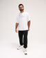 A man modeling a white oversized t-shirt with 'RUDIS' printed in gray outline text on the chest, paired with black pants and white sneakers, against a plain light gray studio background.