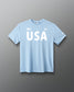 Front view of RUDIS USA Elite Super Soft T-Shirt in light blue, showcasing white USA lettering, American flag graphic, RUDIS Hex logos, and short sleeves.