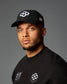 Man wearing a black cap and black shirt with logos on a gray background