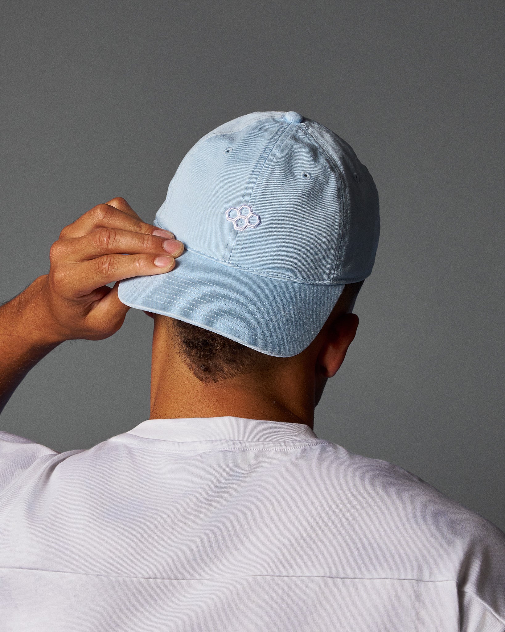 Person wearing a light blue cap with a logo on a gray background