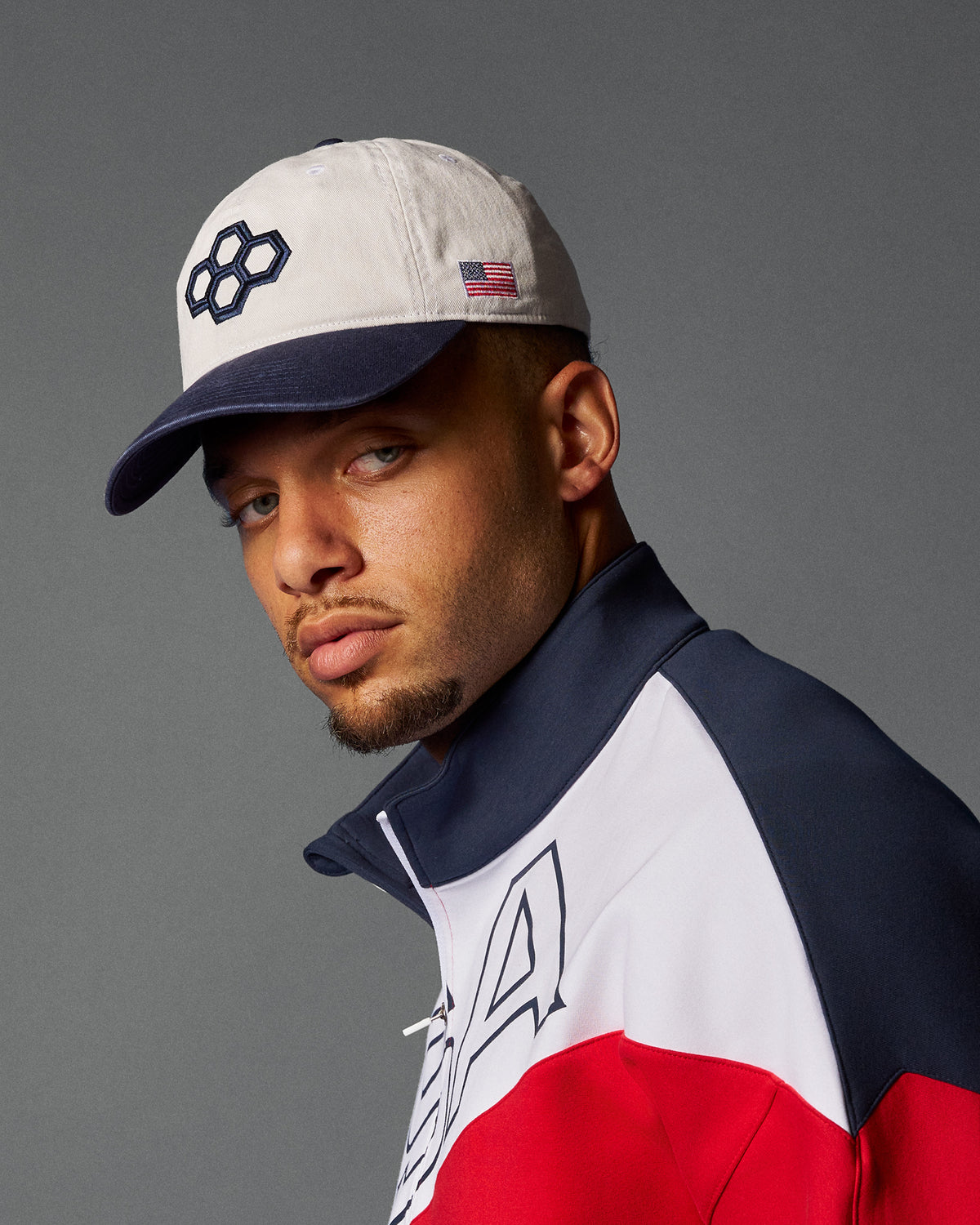 Man wearing a cap and a jacket with a logo on a gray background