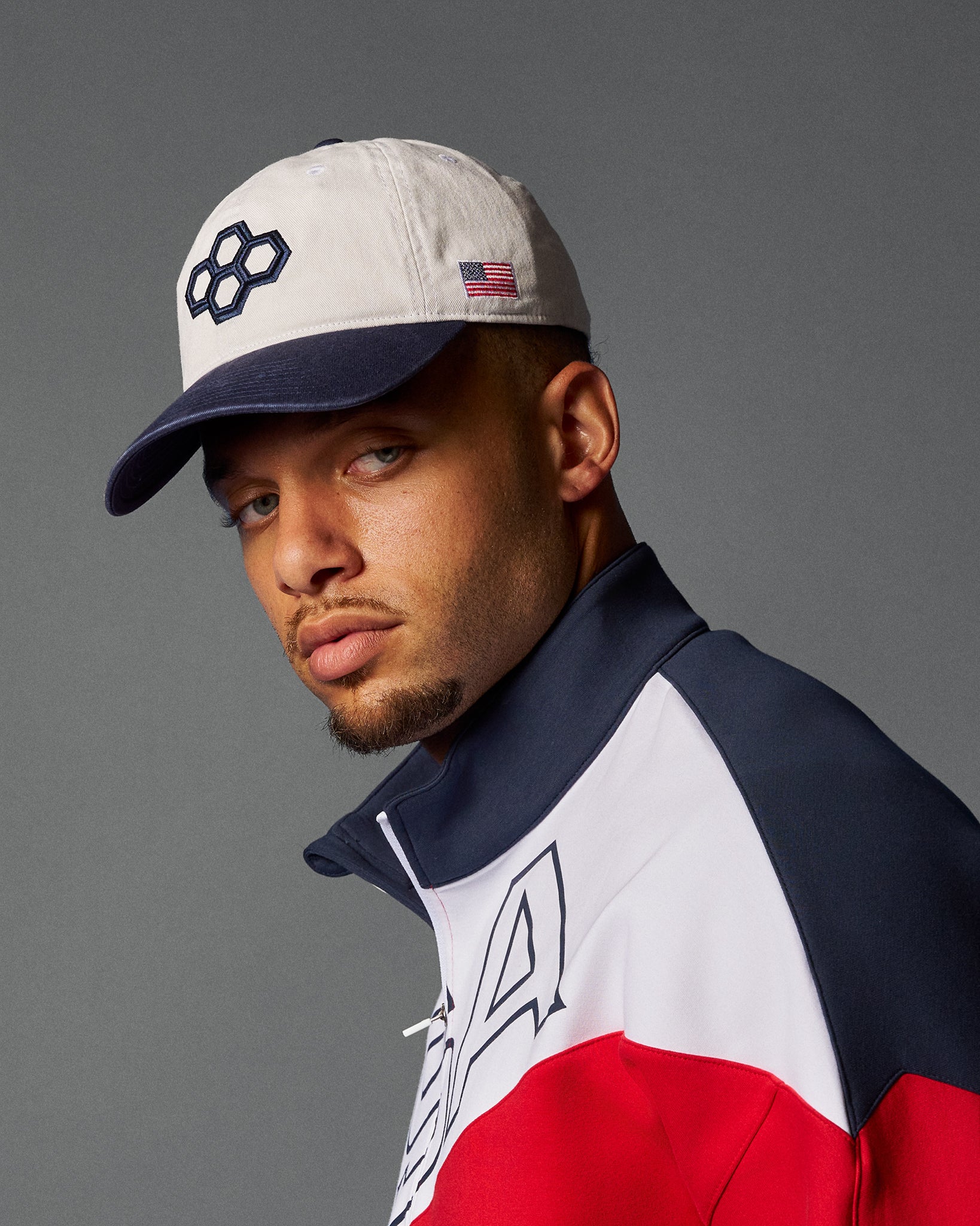 Man wearing a cap and a jacket with a logo on a gray background