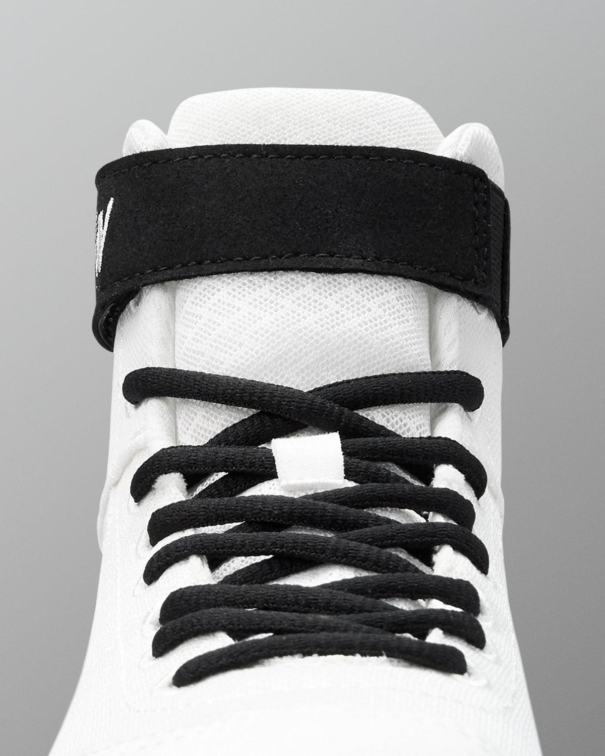 White wrestling shoe with black shoelaces on a gray background