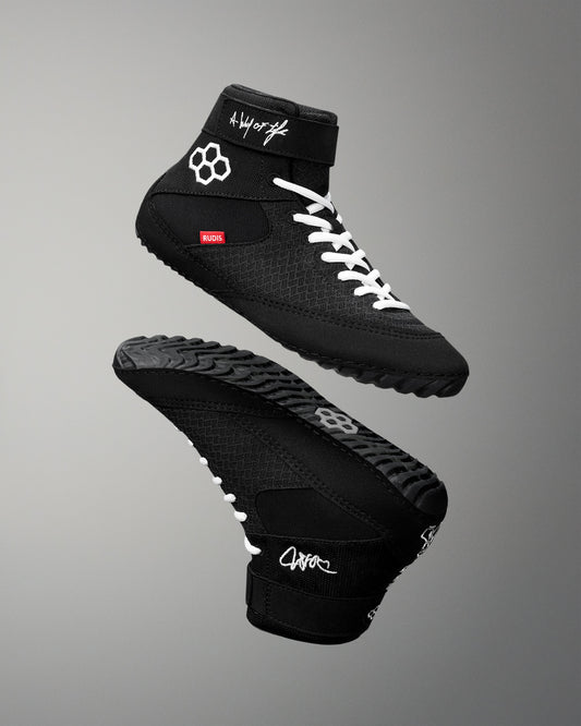 Black wrestling shoes with white laces on a gray background