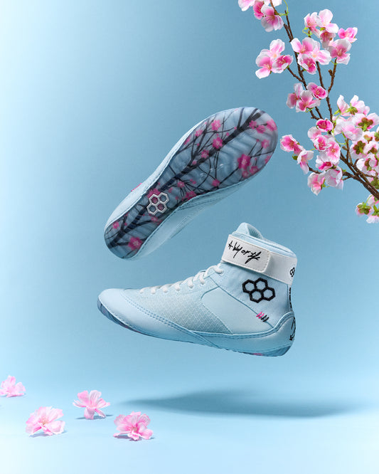 Light blue wrestling shoes with floral design on a light blue background with pink flowers.
