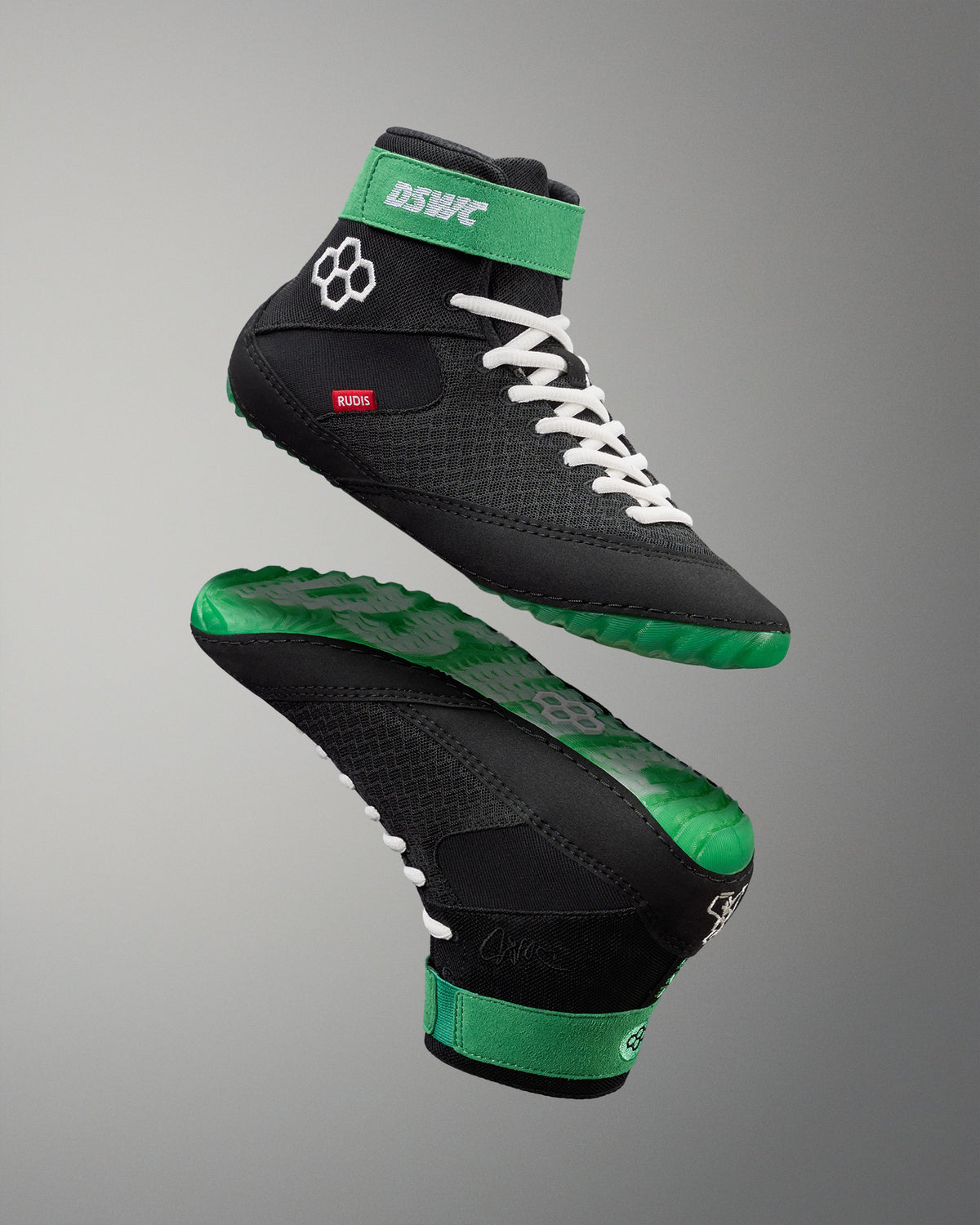 Black and green wrestling shoes with white laces on a gray background