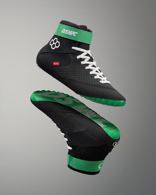Black and green wrestling shoes with white laces on a gray background