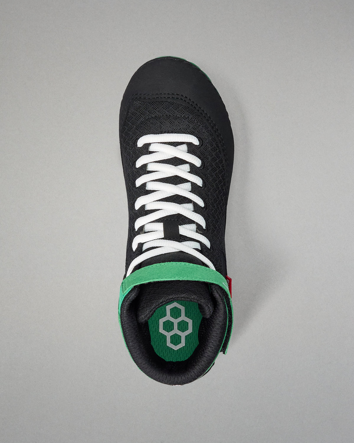 Black wrestling shoe with white laces and green sole on a gray background