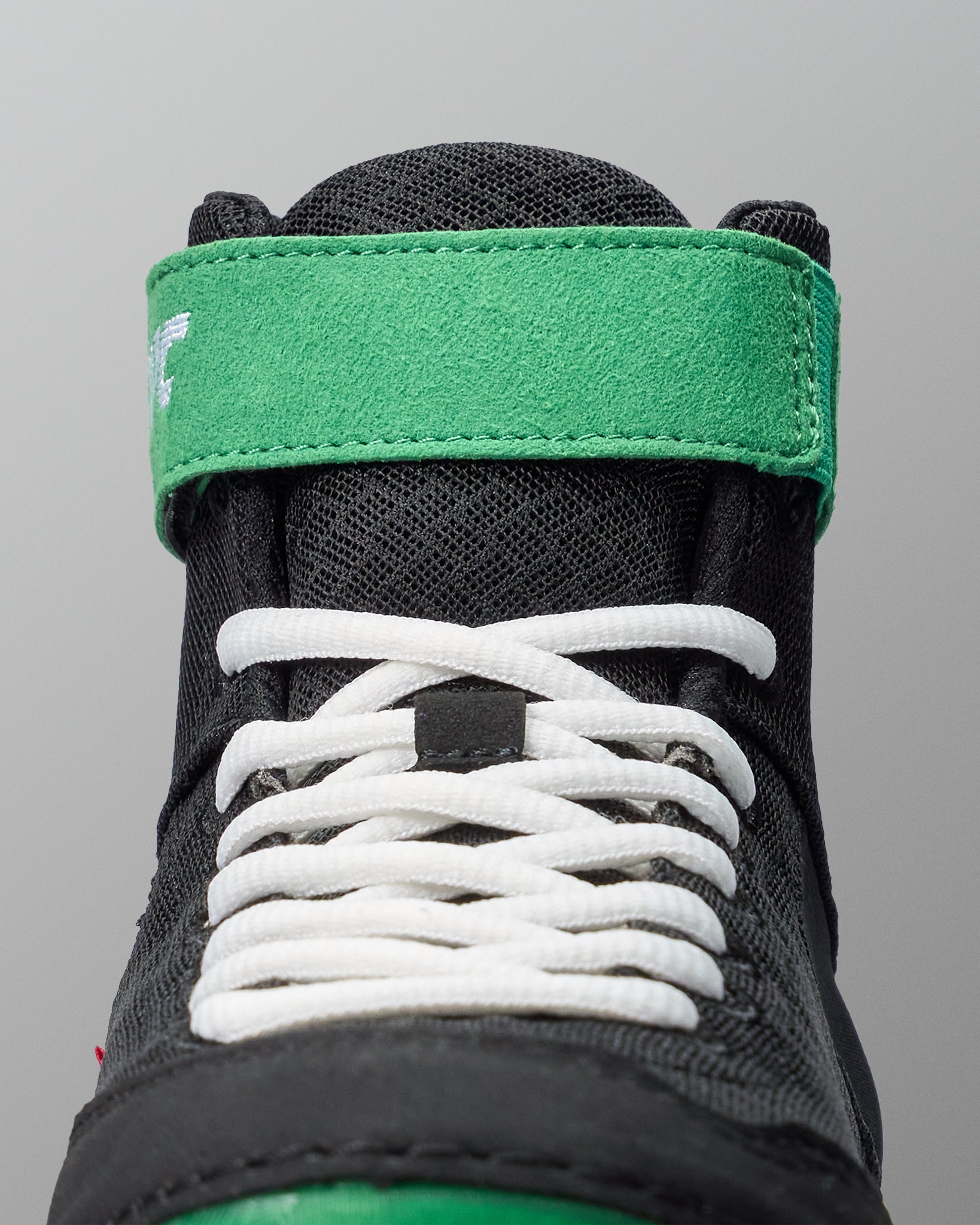Close-up of a black wrestling shoe with white laces and green accents on a gray background