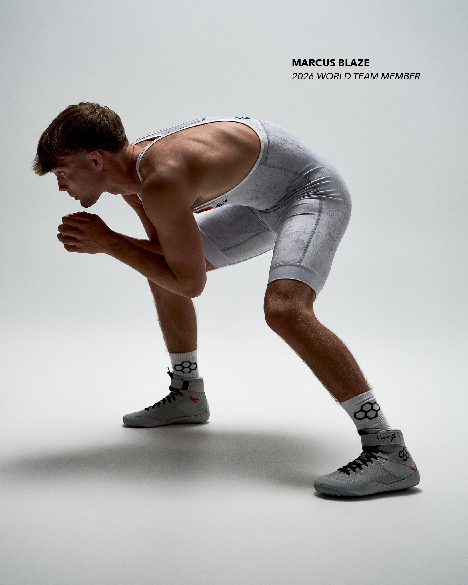 Wrestler, Marcus Blaze, wearing RUDIS Samurai Speed Adult Wrestling Shoes in Kokoro with a white wrestling singlet, demonstrating the high-top design in a low wrestling stance.
