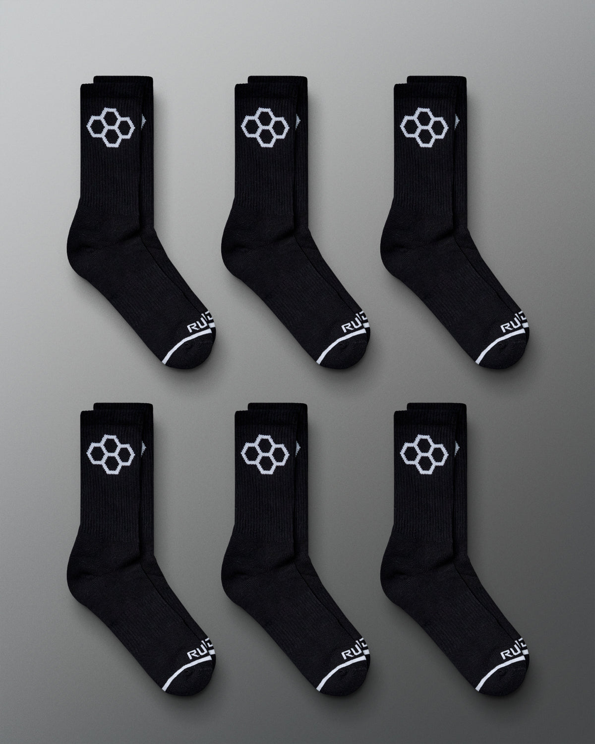 A display of six pairs of black athletic socks featuring a distinctive white hexagonal logo and stylish design details laid out on a gray background