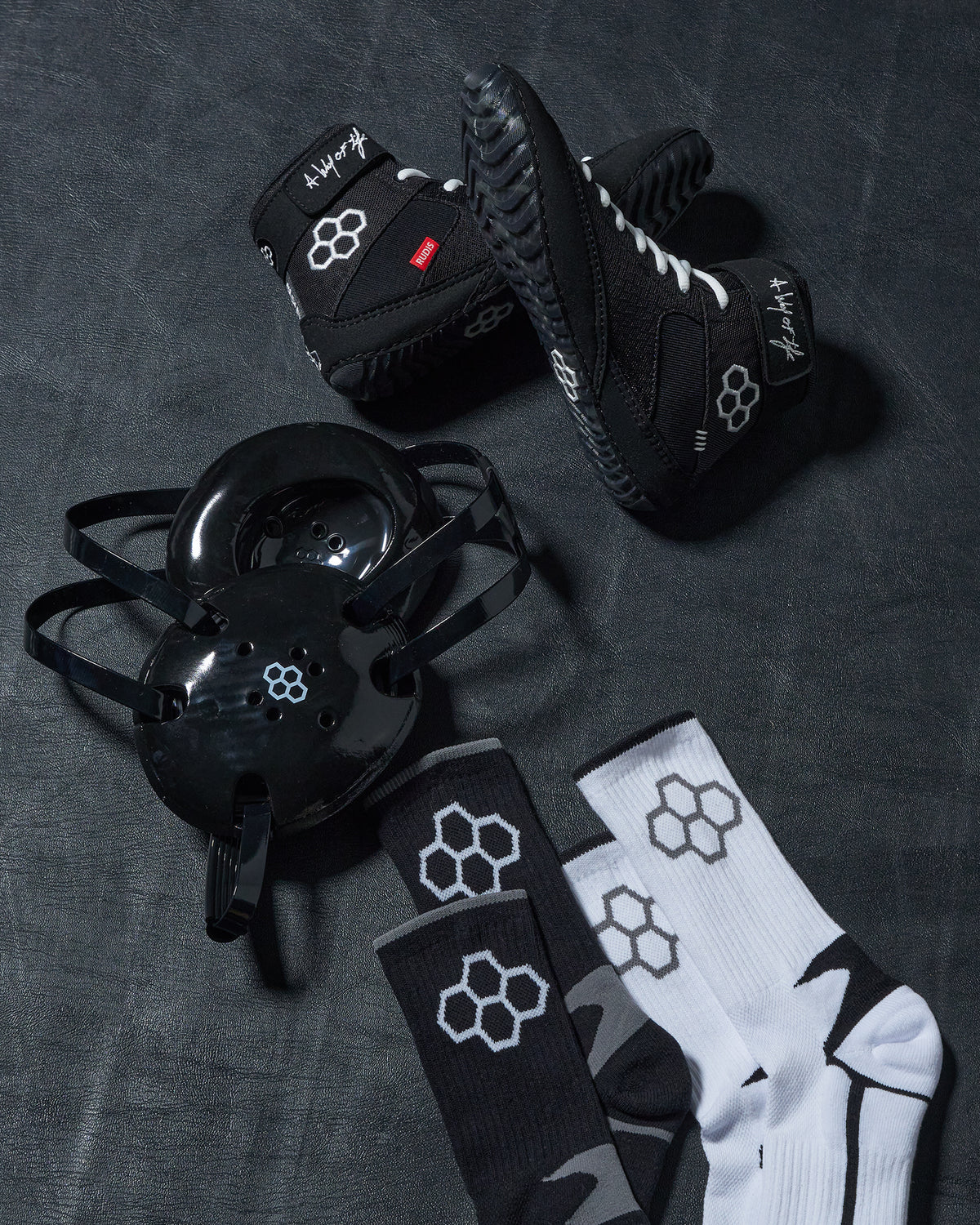 Black wrestling shoes, headgear, and socks with a logo on a dark textured surface