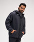 A man wearing a Black quilted puffer jacket with a white geometric logo on the chest, standing against a light gray studio background.
