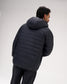 A man wearing a black quilted puffer jacket with a hood, shown from a rear three-quarter angle against a light gray studio background.